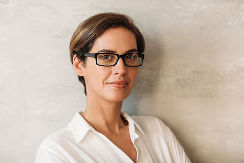 Portrait of a beautiful woman in eyeglasses leaning against a wall and looking at camera. Business female with short hair looking at the camera.