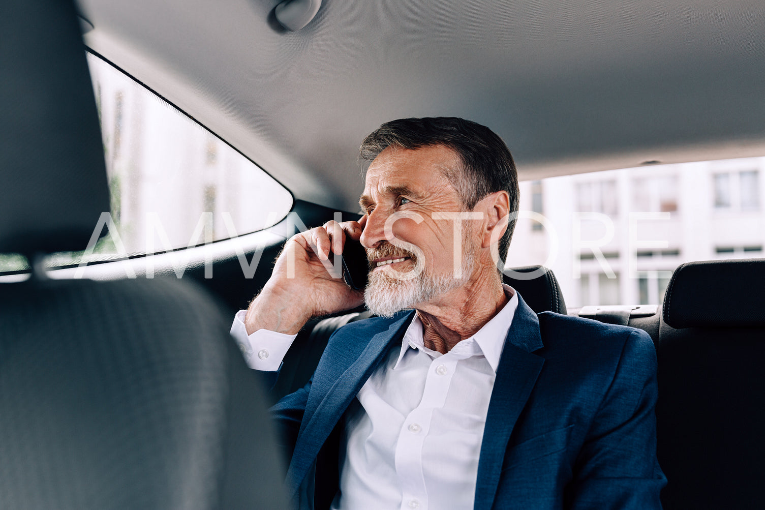 Smiling businessman talking on a cell phone while sitting on a backseat of a taxi	