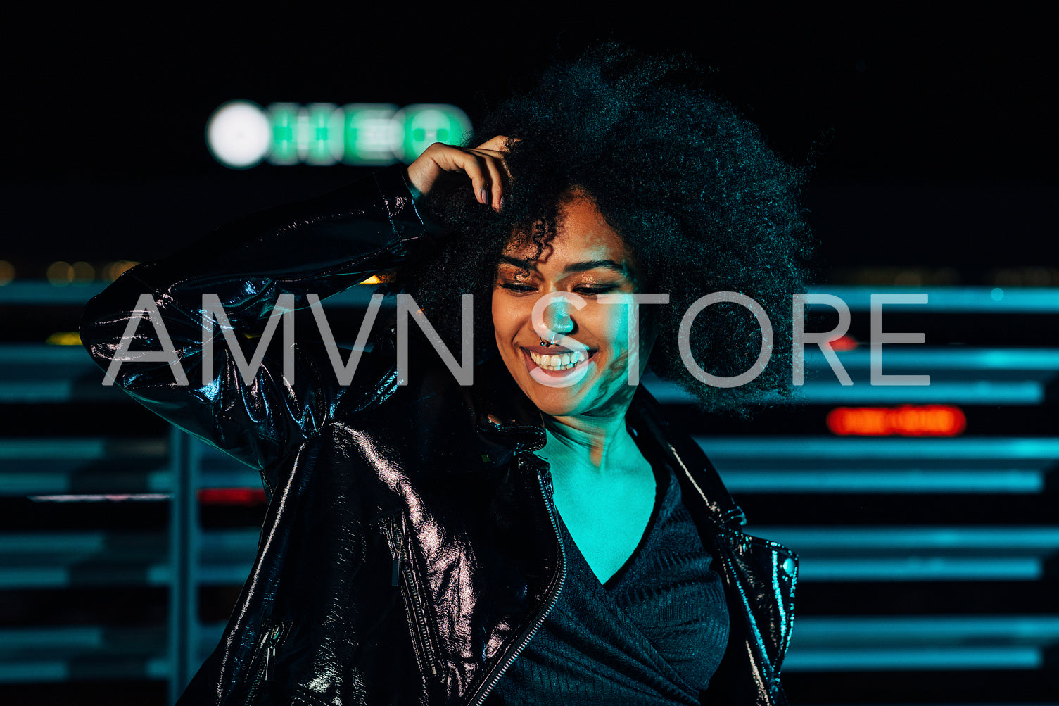 Smiling woman posing under colored light at night and looking down	