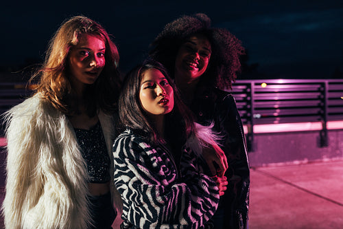 Thee stylish girls looking at camera under pink neon light