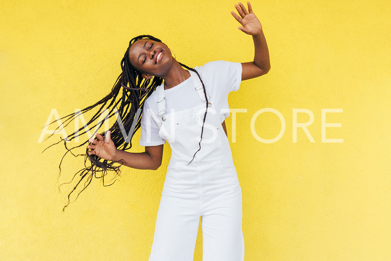 Cheerful woman wearing white overall dancing at yellow wall