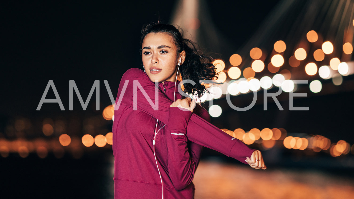 Young fitness woman in headphones stretching her arm at night during a workout