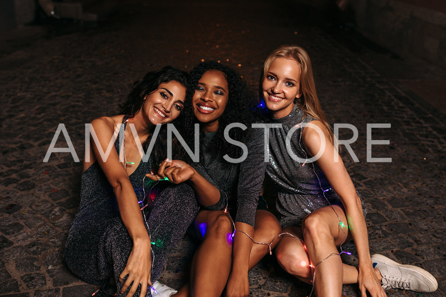 Happy friends sitting on sidewalk at night, looking at camera	