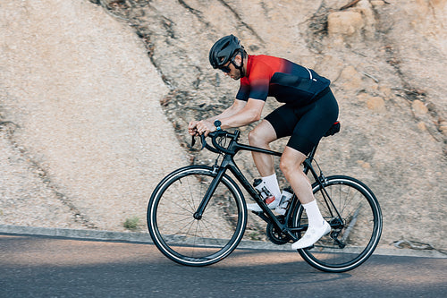 Male cyclist riding up on a road. Professional cyclist in sportswear doing intense training outdoors.