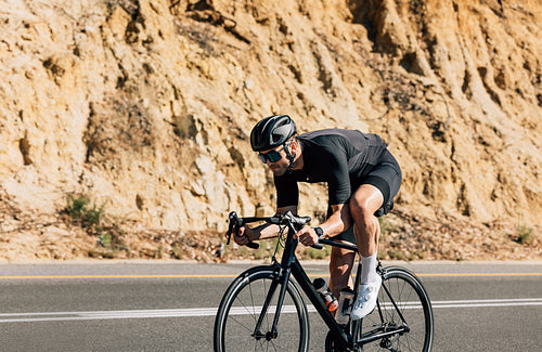 Side view of a professional male cyclist riding on a road. Strong cyclist on a countryside highway.