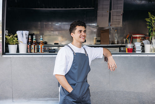 Side view of smiling waiter standing at food truck and looking away