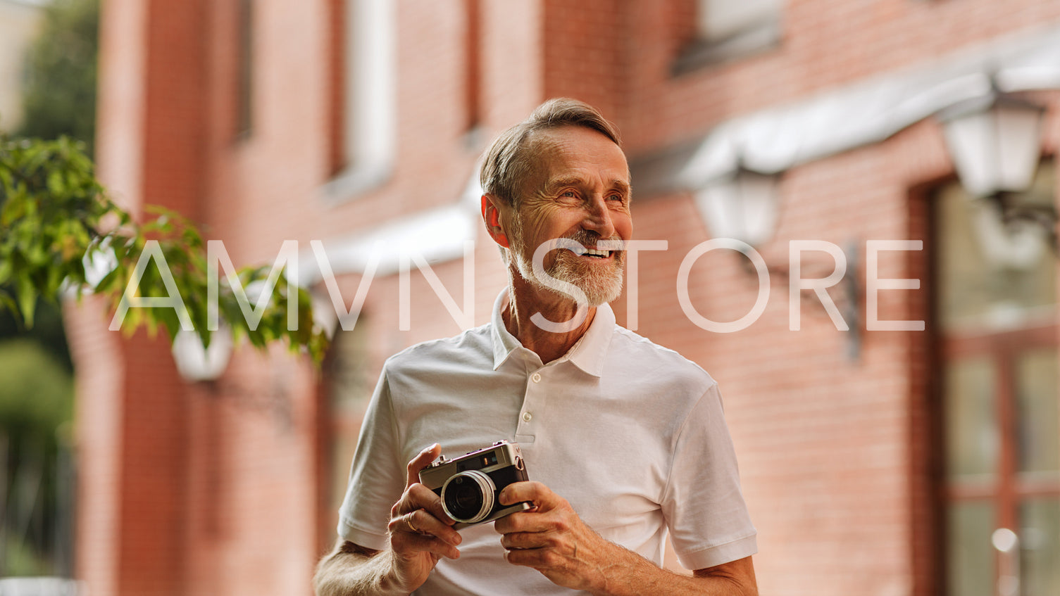 Smiling tourist looking away. Senior man standing outdoors with a film camera outdoors.	