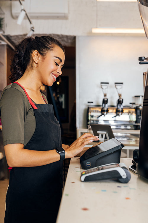 Side view of female waitress using cashbox computer in cafe. Woman touching a display of a electronic cash register.