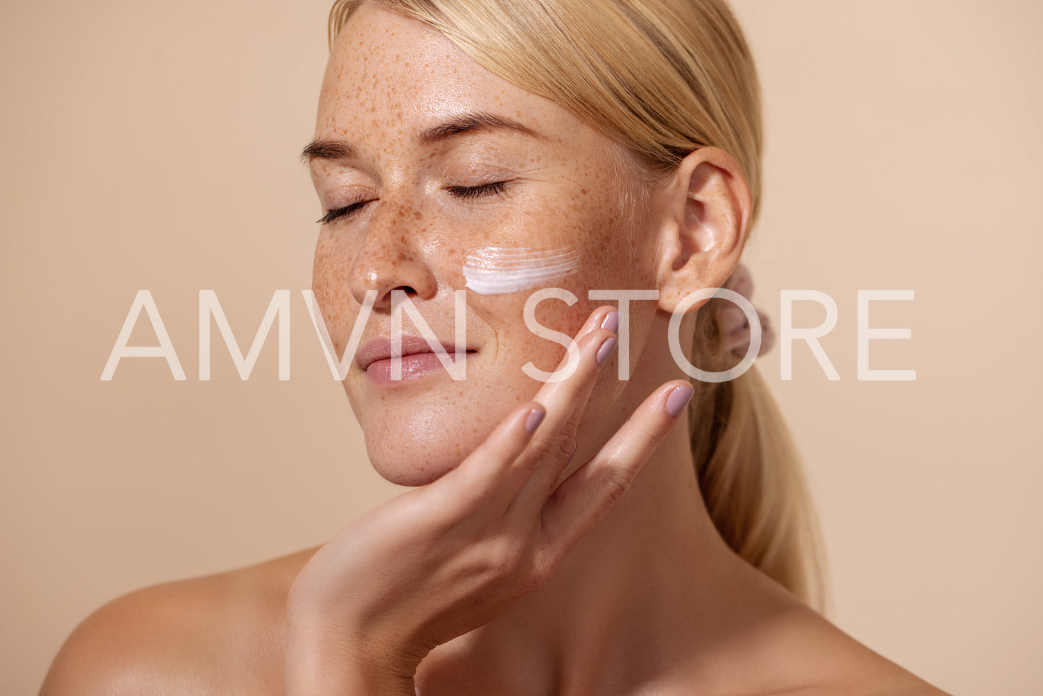 Close up of beautiful young female with cream on a face. Smiling woman with closed eyes touching cheek with fingers.