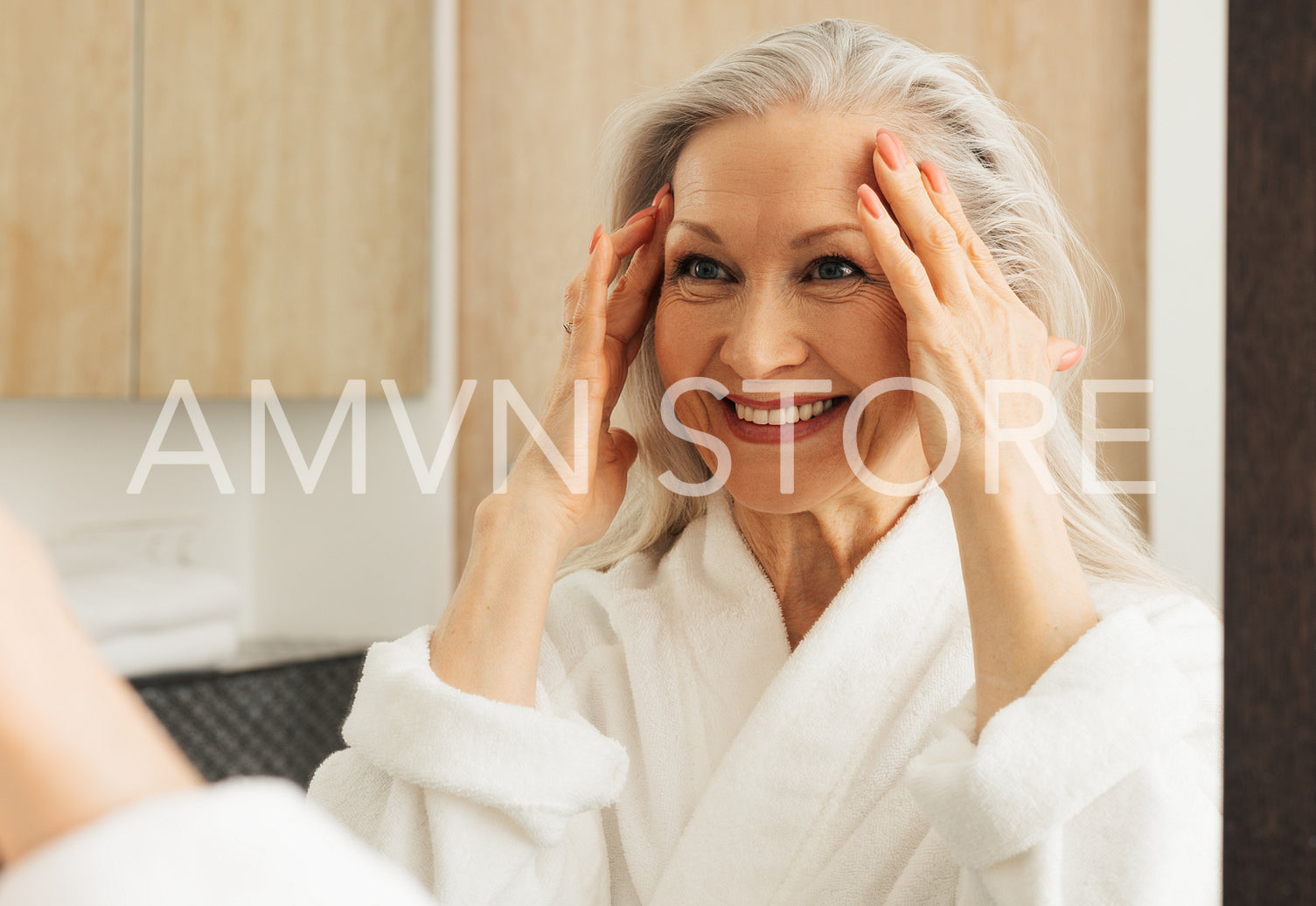 Happy senior woman with grey hair looking at a mirror and touching her face while looking at mirror