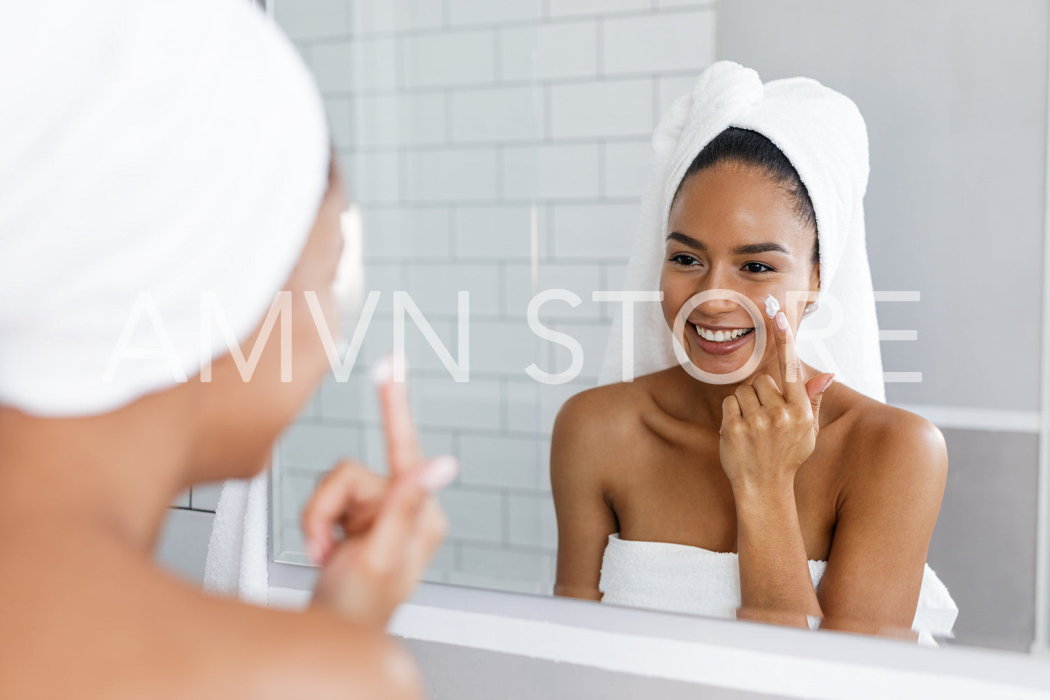 Portrait of a young smiling woman applying moisturiser to her face in the bathroom	