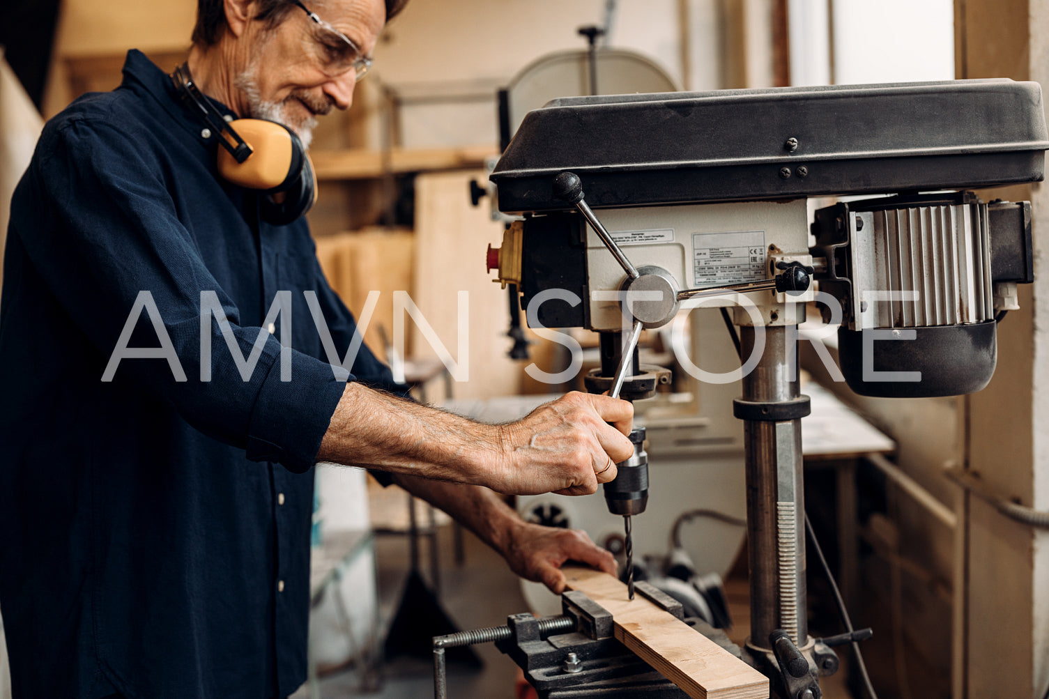 Mature worker in carpentry preparing furniture parts using a drilling machine	