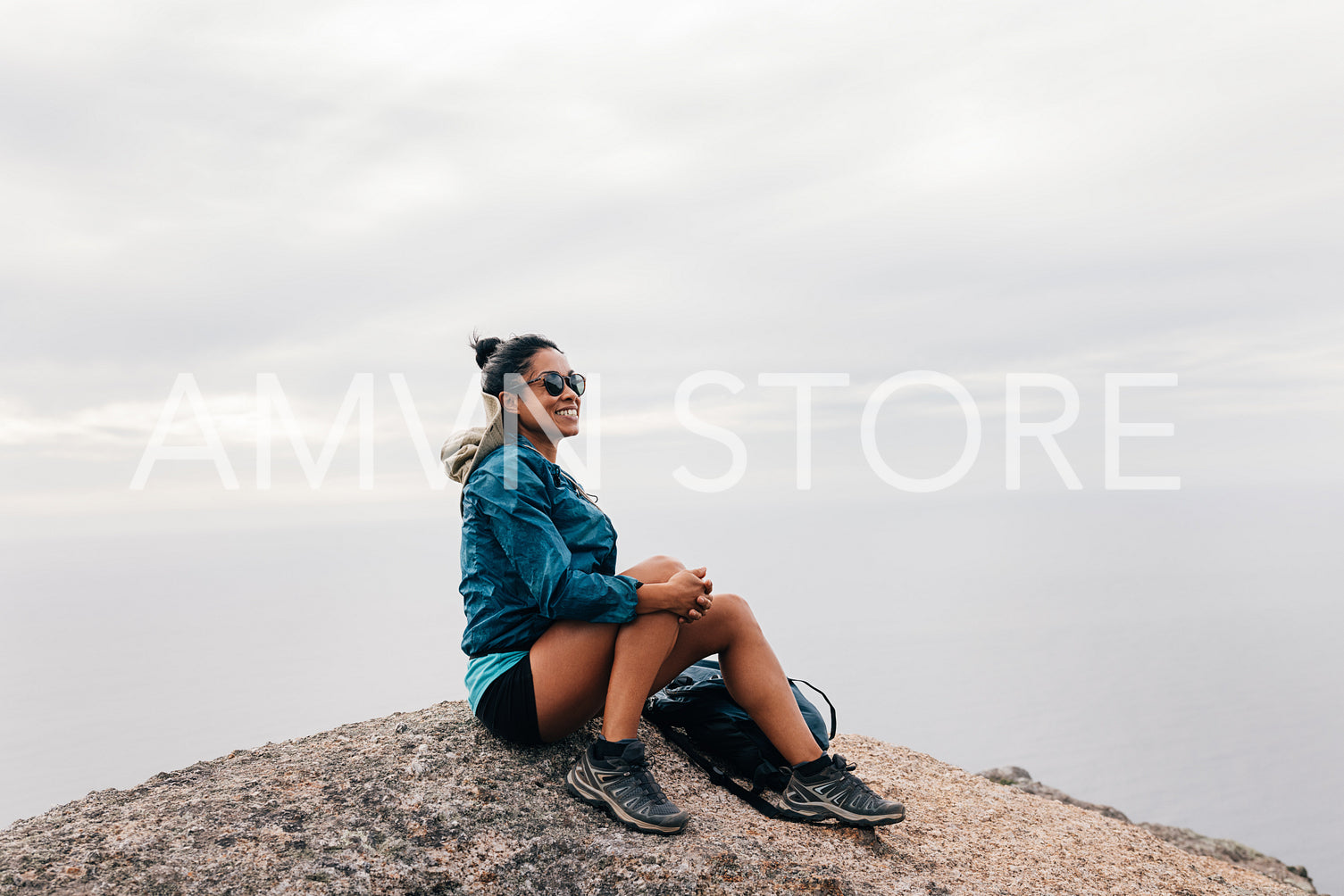 Smiling woman sitting on the cliff looking at the view. Female hiker resting on a rock looking away.