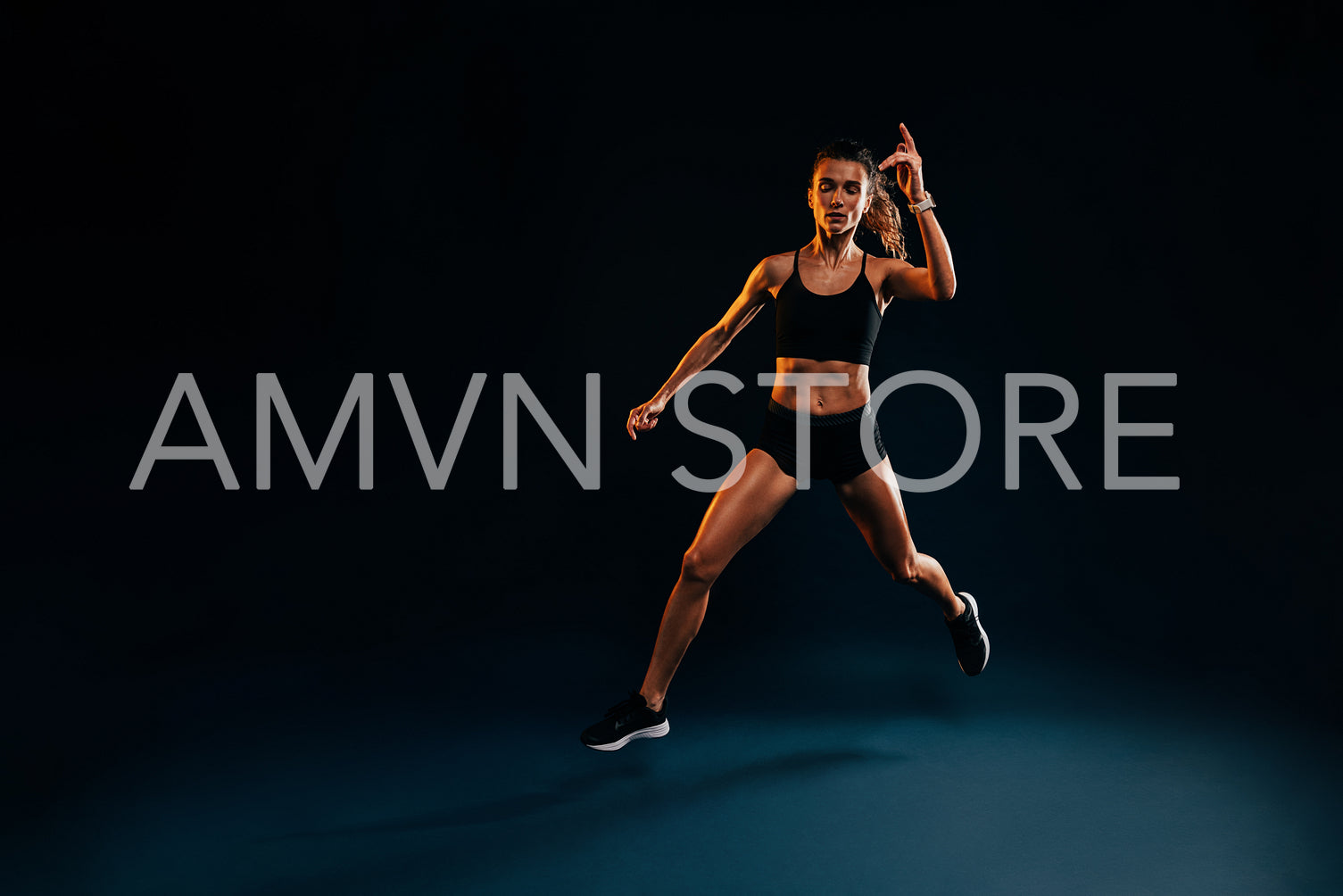 Young woman runner jumping in studio. Muscular athlete exercising on black backdrop.