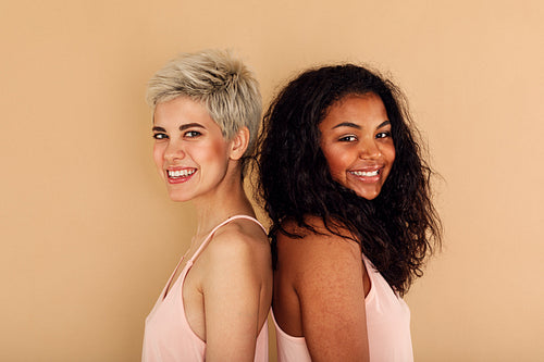 Two happy women posing back to back in studio