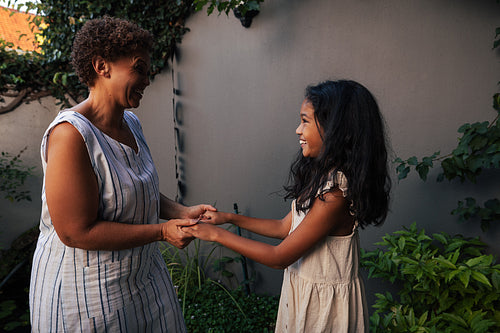 Granny and granddaughter standing together in the backyard holding hands and looking at each other. Kid and grandma spending time together.