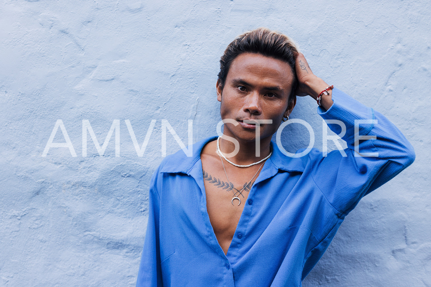 Young handsome male in a blue shirt adjusting his hair leaning on a wall