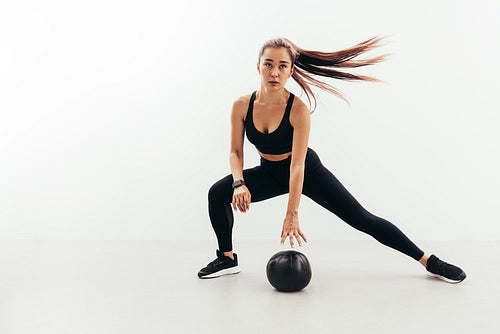 Young fit woman in sports clothes doing warming up exercises with a medicine ball