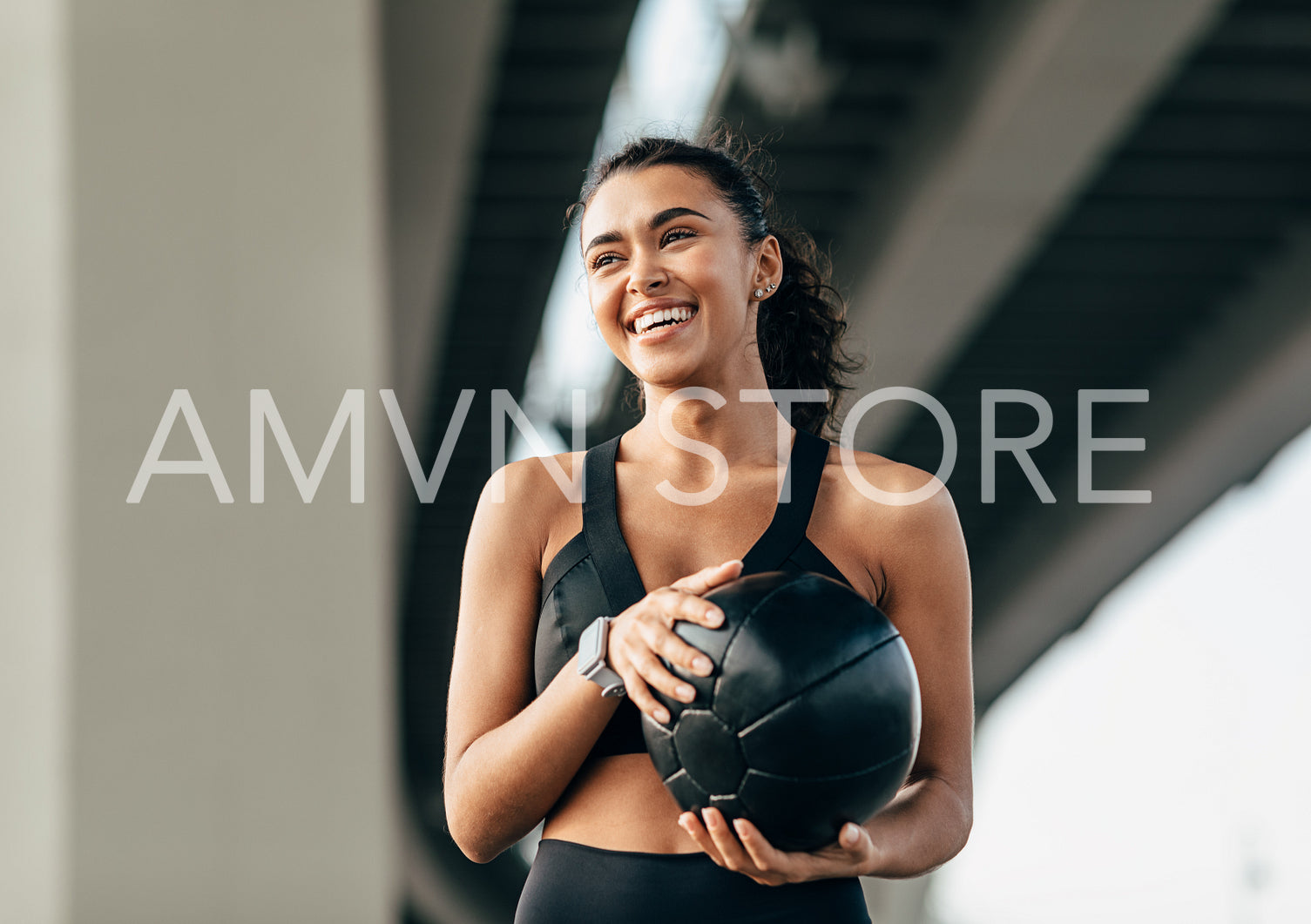 Beautiful woman holds a medicine ball standing under highway relaxing during training	