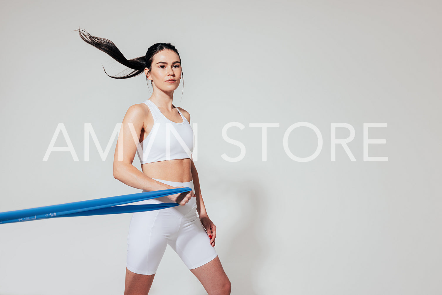 Confident woman in fitness wear with resistance band over white backdrop