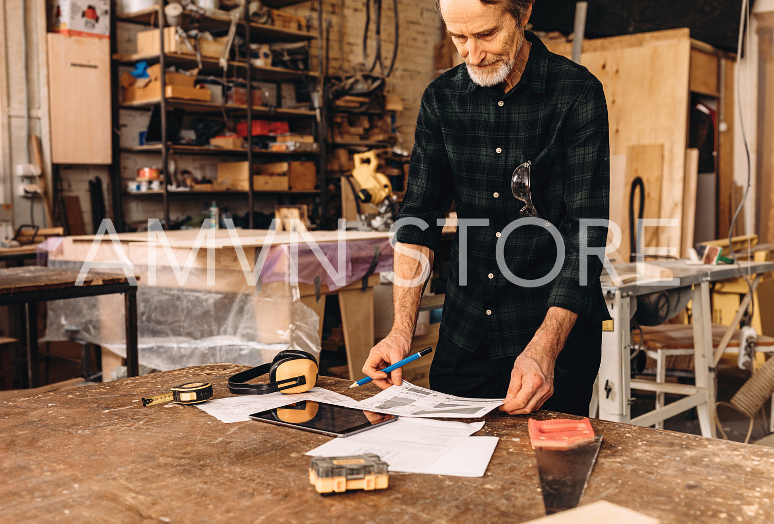 Male carpenter standing at workbench and reading document	