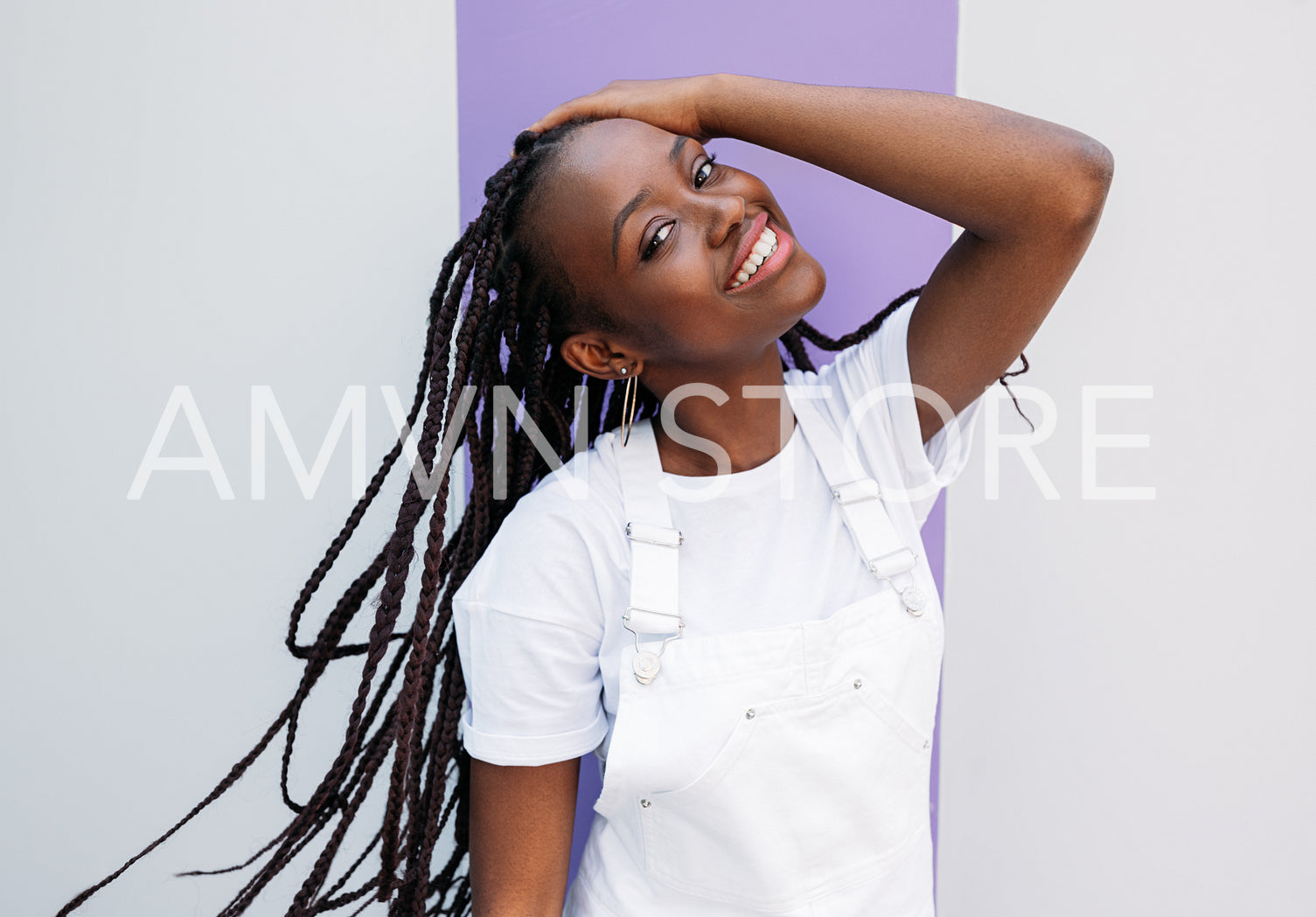 Happy girl in white overall adjusting her long braids and looking straight at a camera