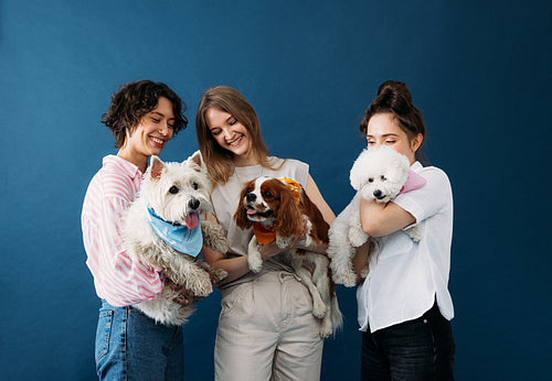 Three young women holding their cute little dogs while standing