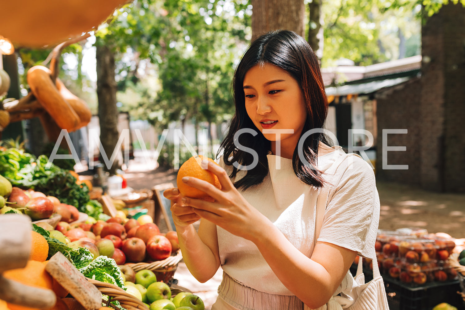 Young woman holding an orange while standing at a stall on a street market