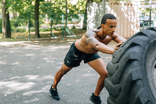 Young muscular man pushing large tire on sports ground