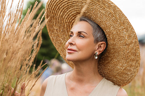 Close-up mature female with short grey hair wearing a straw hat looking at wheat