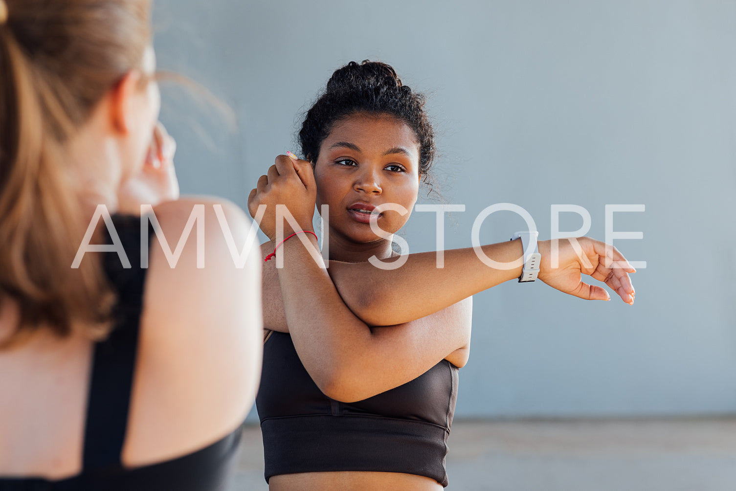 Female with curly hair stretching her hand before training while standing outdoors with her friend