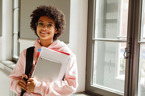 University student with books standing indoors at window