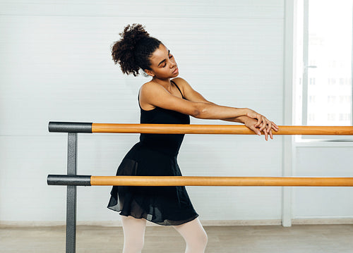 Young woman standing with closed eyes and leaning on barres at the dance studio