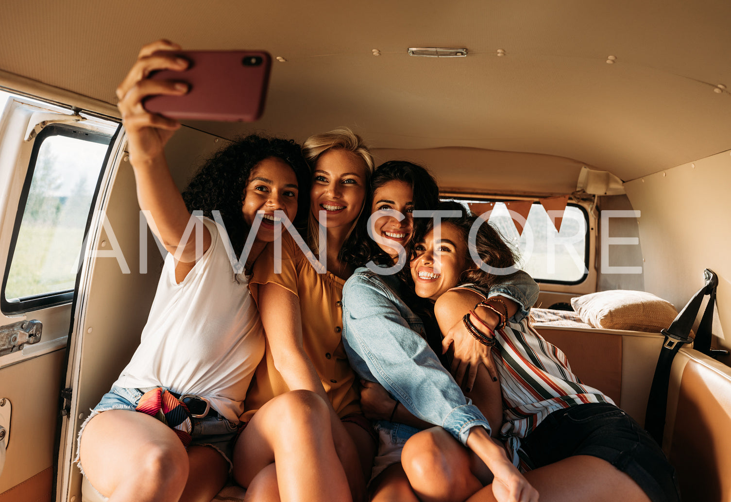 Four beautiful friends taking selfie in a van during a road trip. Smiling women on vacation.