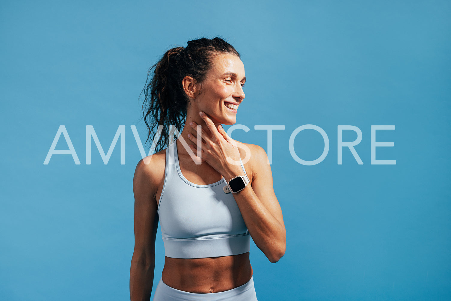 Smiling woman in fitness wear touching her neck and looking away on blue background