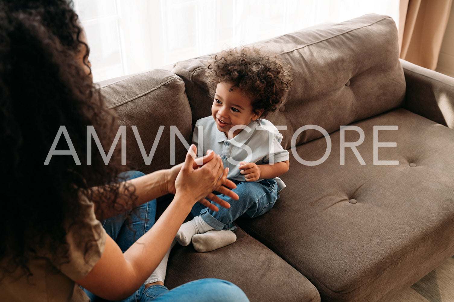 Son and mother sitting on a sofa in living room and playing	