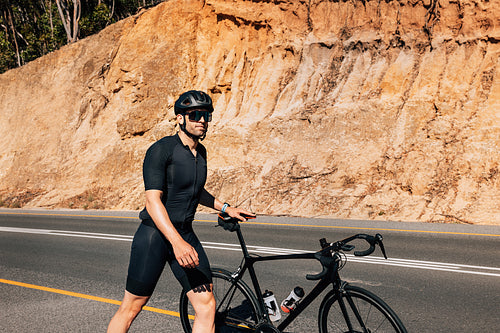 Professional cyclist walking with his road bike on a roadside