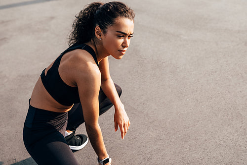 Side view of a muscular sportswoman sitting outdoors resting during training and looking away