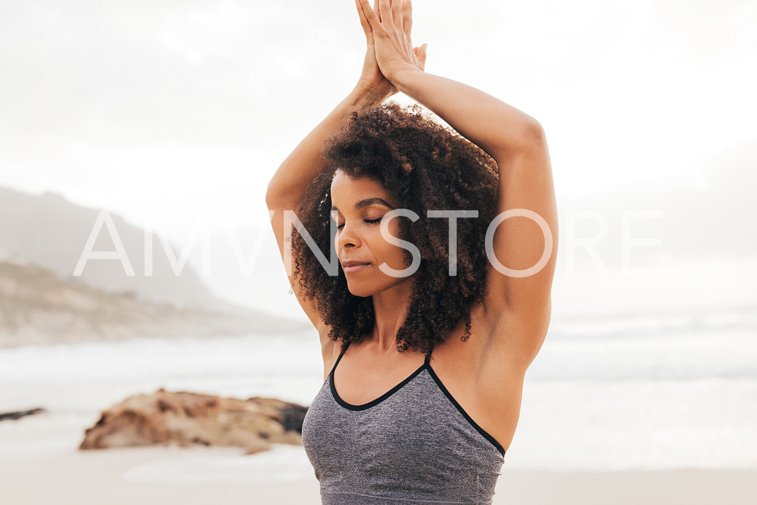 Cropped shot of a young woman with folded hands above her head meditating outdoors on a beach