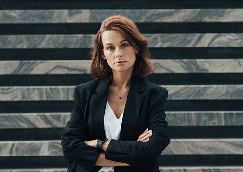 Confident middle-aged businesswoman with crossed arms. Female with ginger hair in formal wear looking at the camera.