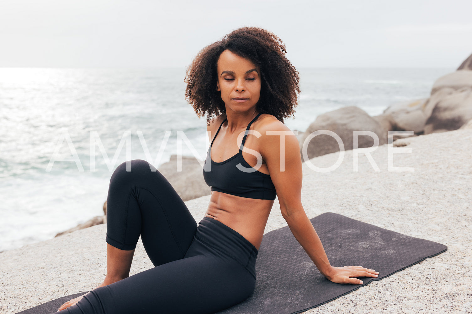 Fit woman with closed eyes sitting on mat by ocean relaxing after yoga training