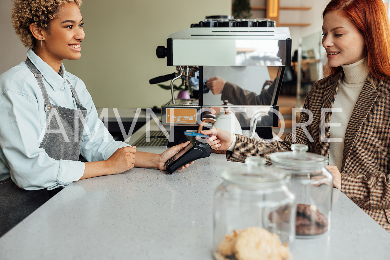 Client paying by card at a coffee shop. Smiling barista holding pos terminal while customer paying.