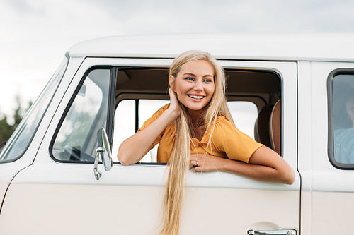 Happy woman with long hair looks out of car window while sitting on driver seat