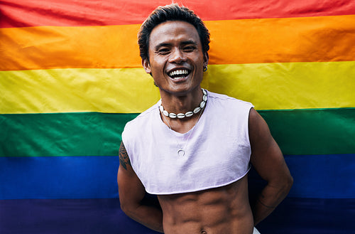 Happy guy posing on LGBT flag. Laughing male standing against rainbow flag.