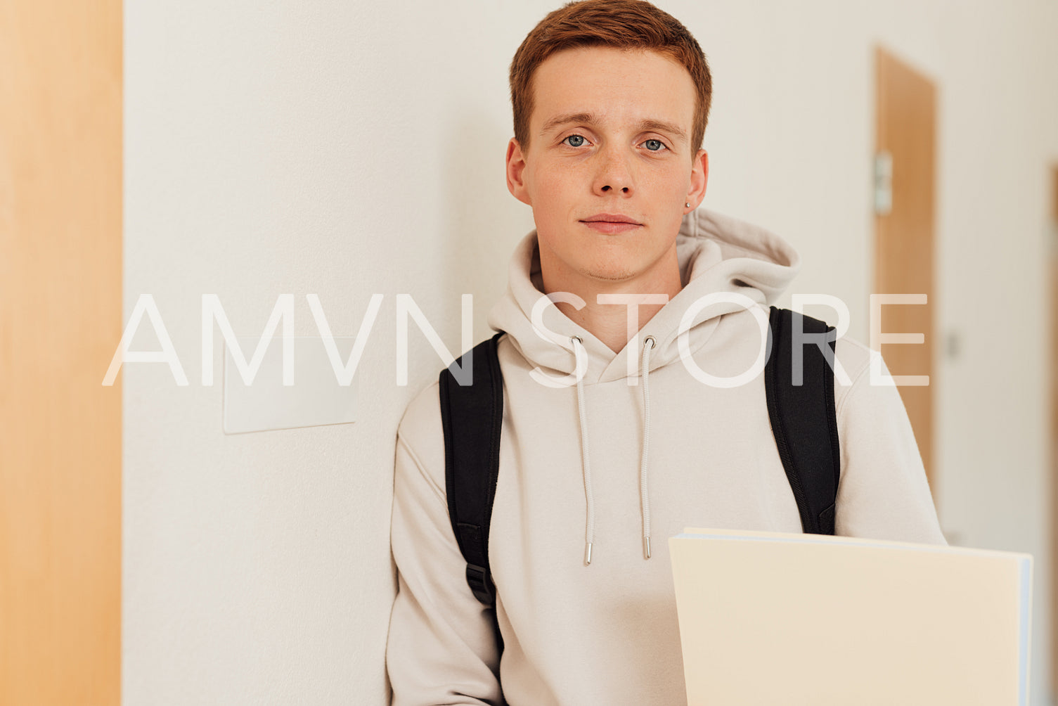 Portrait of handsome male student at wall. Guy in casuals holding a textbook looking at camera.