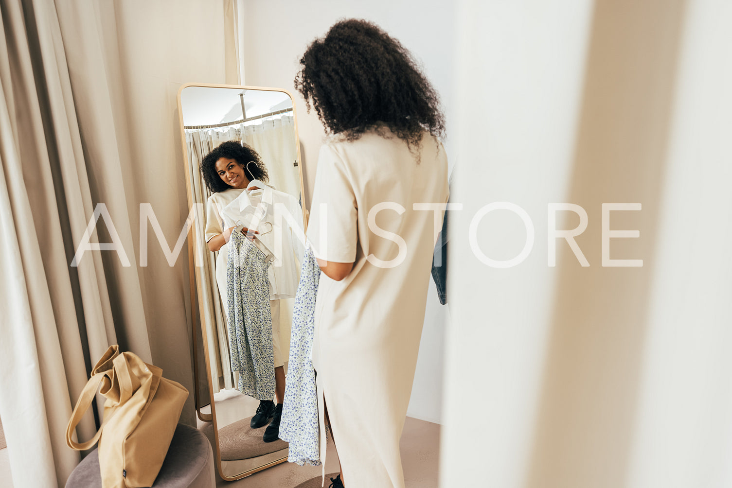 Young stylish woman in fitting room looking at mirror trying on new clothes