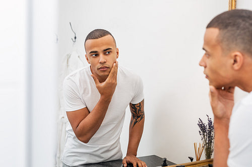 Portrait of a handsome young man examining his face in the bathroom mirror