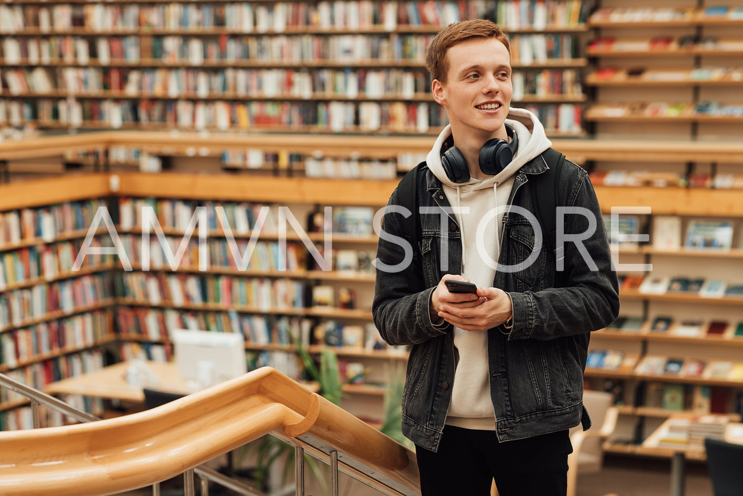 Smiling student with headphones and smartphone standing in university library