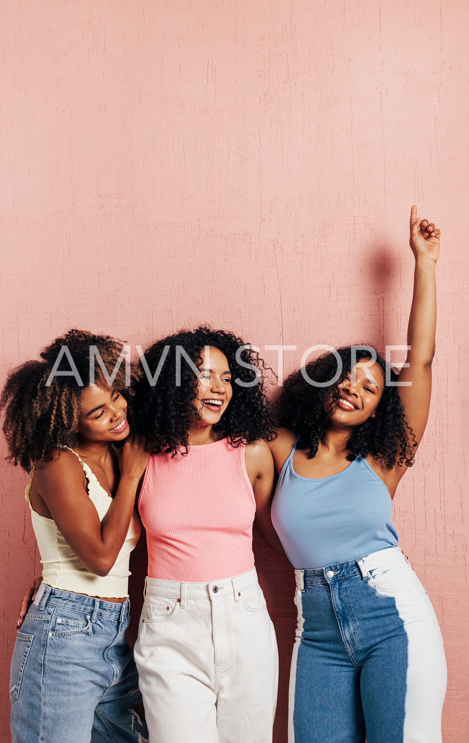 Three beautiful female friends in bright casuals having fun while leaning pink wall