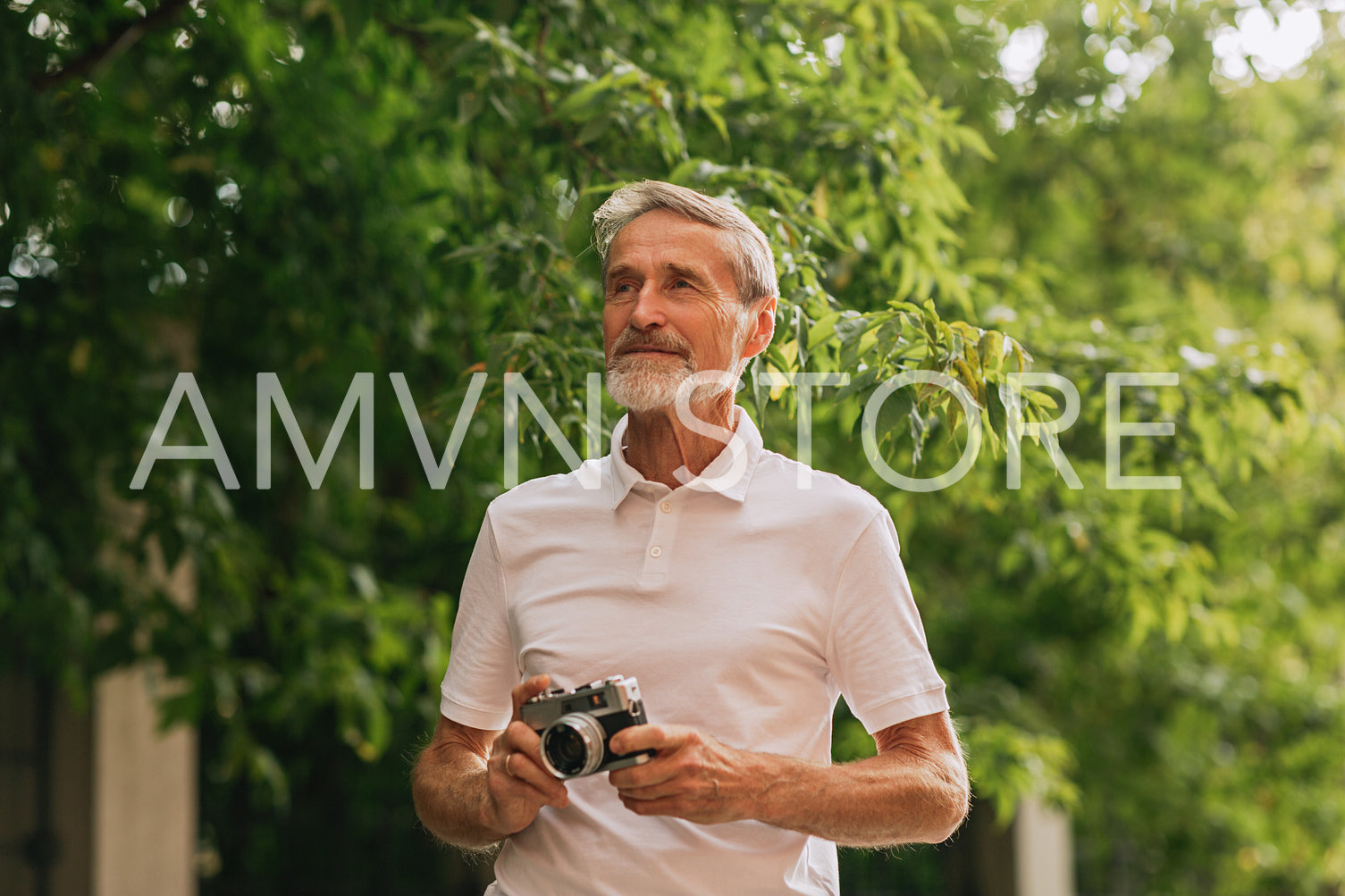 Mature photographer standing outdoors with a film camera and looking away	